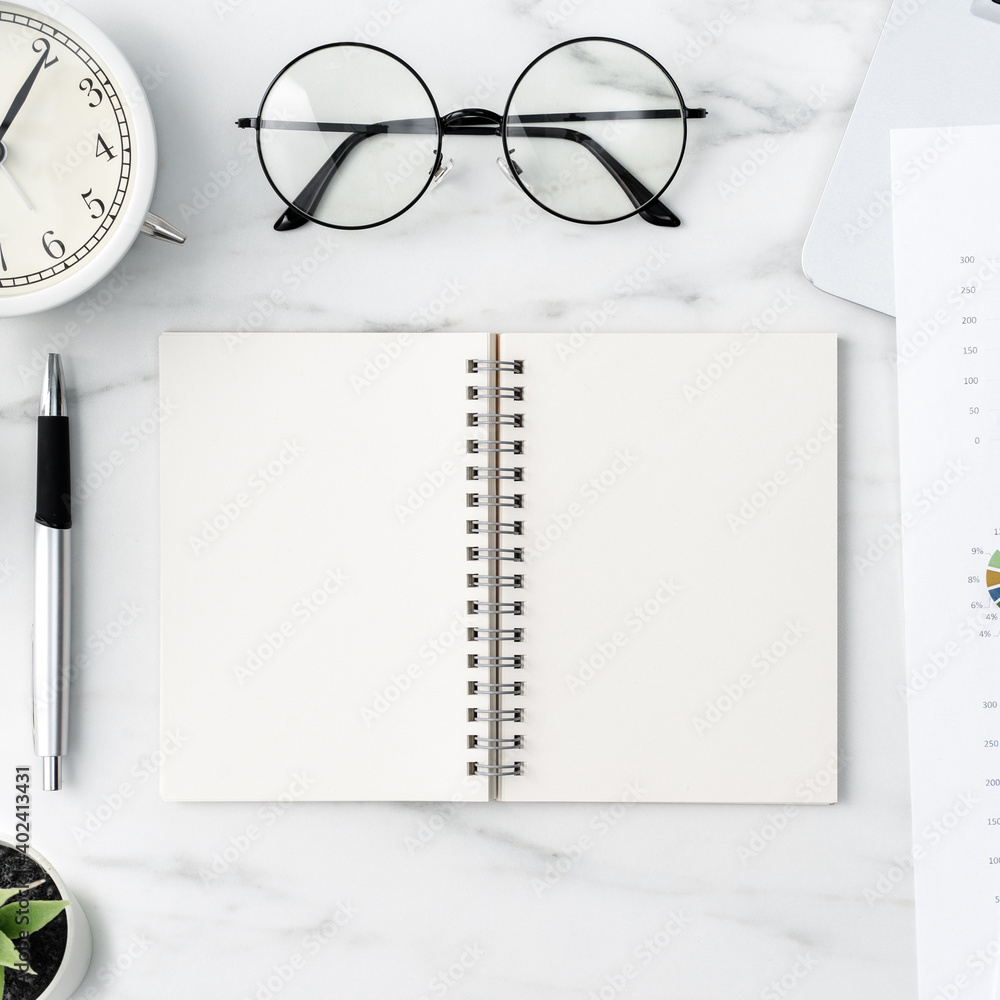 Office table desk work with blank notebook, report and alarm clock on marble white background.