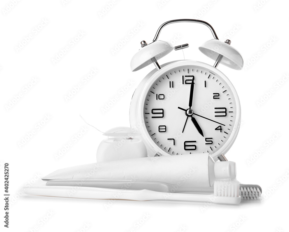 Alarm clock, paste and toothbrushes on white background