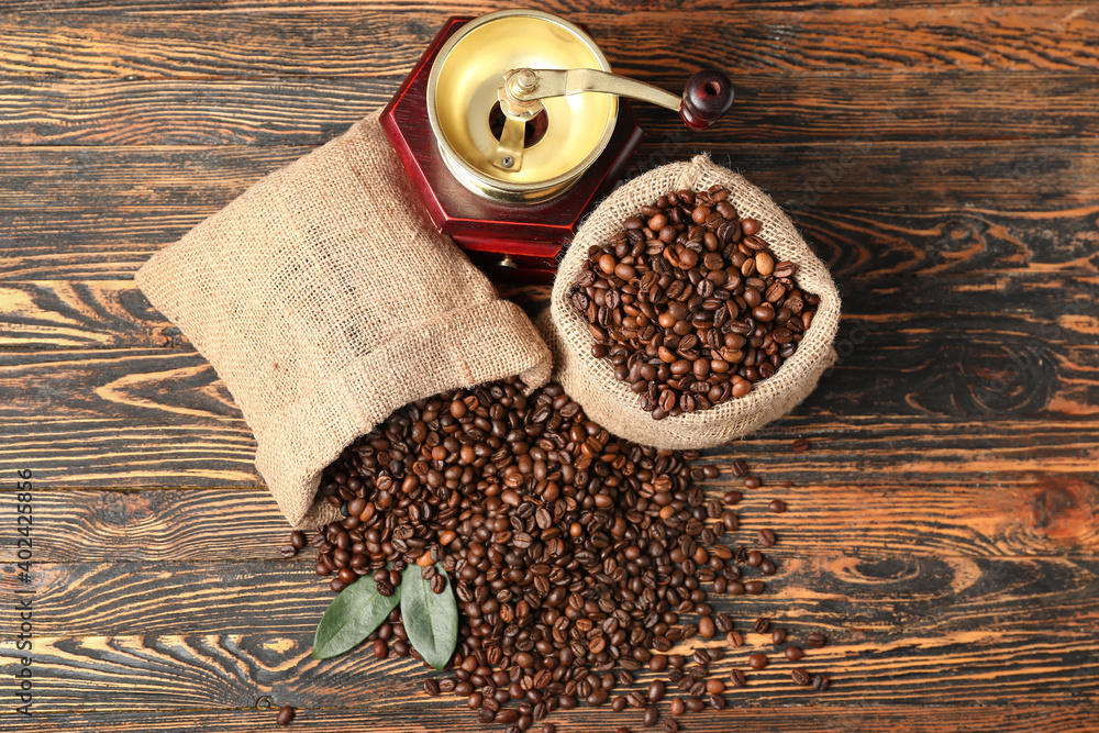 Bags with coffee beans and grinder on wooden background