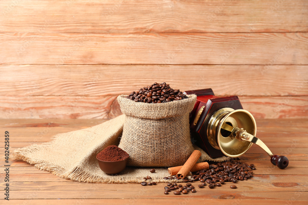 Bag with coffee beans and grinder on wooden background