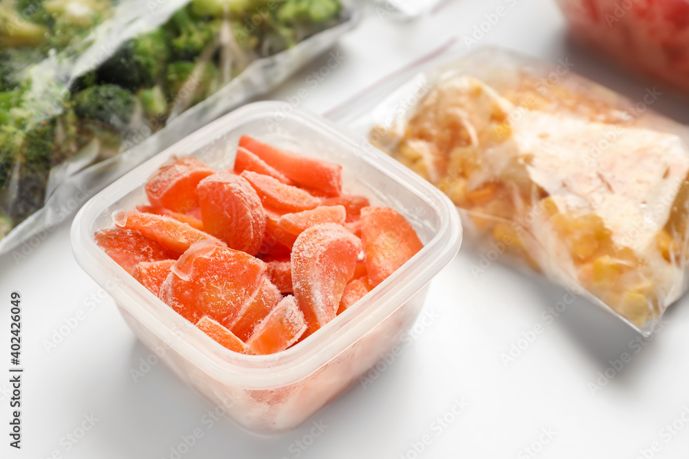 Container and plastic bags with frozen vegetables on white background