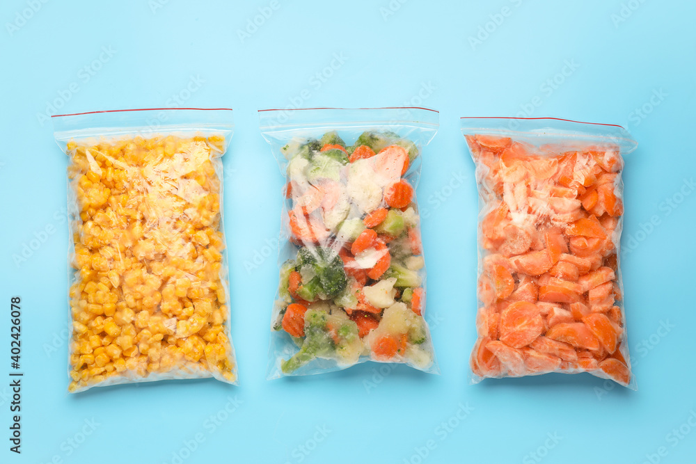 Plastic bags with frozen vegetables on color background