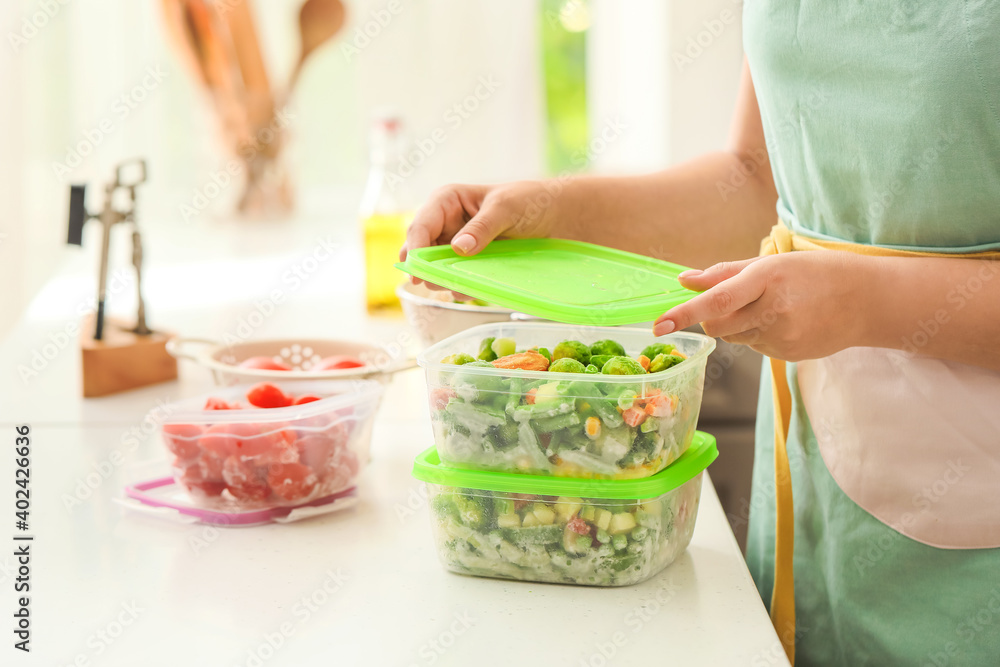 Woman holding plastic containers with frozen vegetables in kitchen