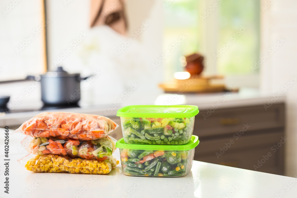 Plastic containers and bags with frozen vegetables on table