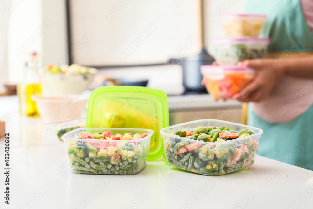 Woman holding plastic containers with frozen vegetables in kitchen