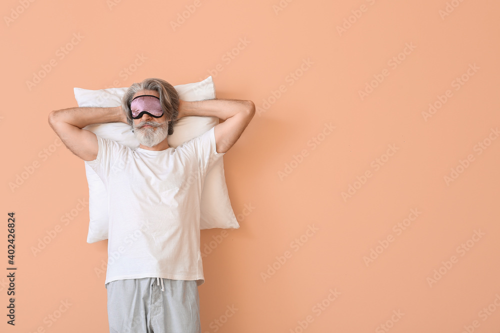 Mature man in sleep mask on color background