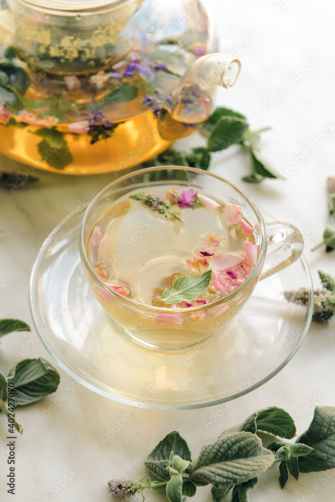 Teapot and cup with herbal tea on light background