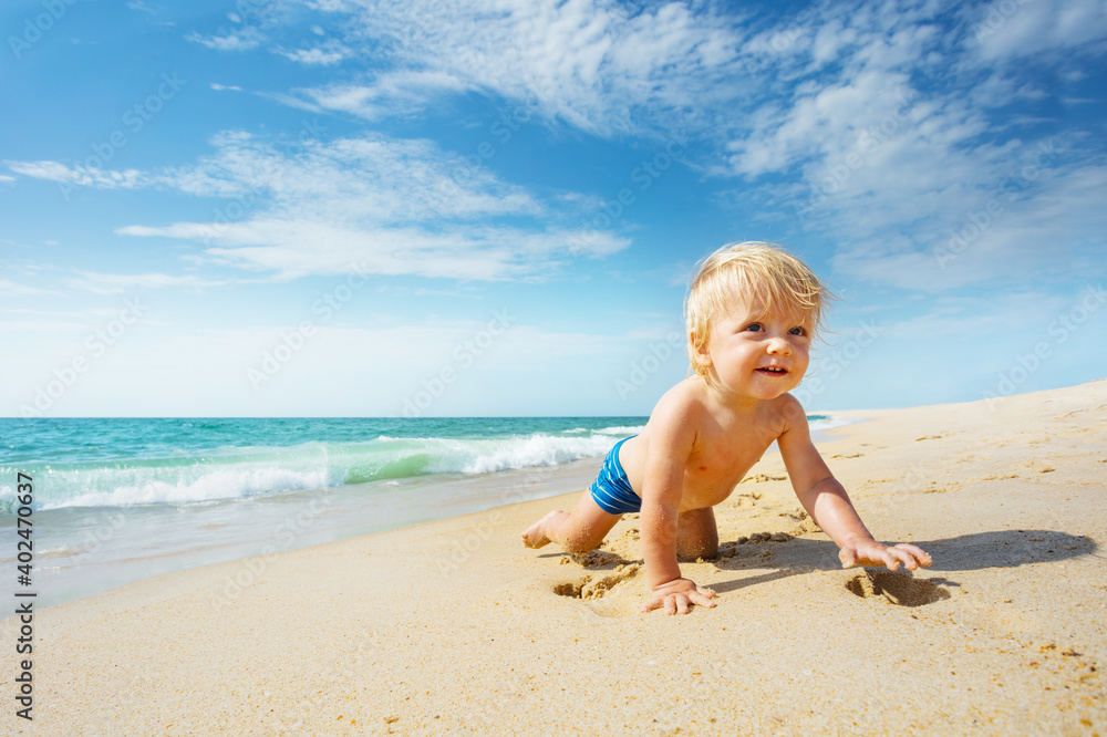 Happy smiling little toddler crawl on the sand near the sea exploring the beach