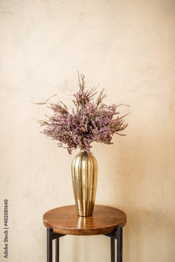 Dried Calluna flower in a gold vase on a beige wall background