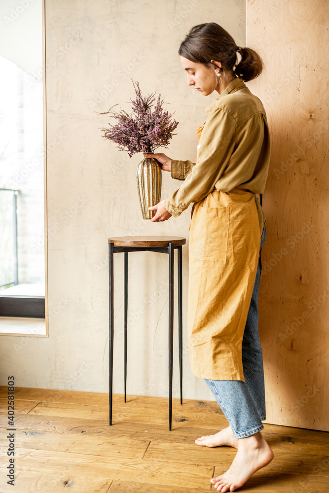 一位女士在米色墙壁背景上的金色花瓶里用一朵干卡卢纳花装饰家