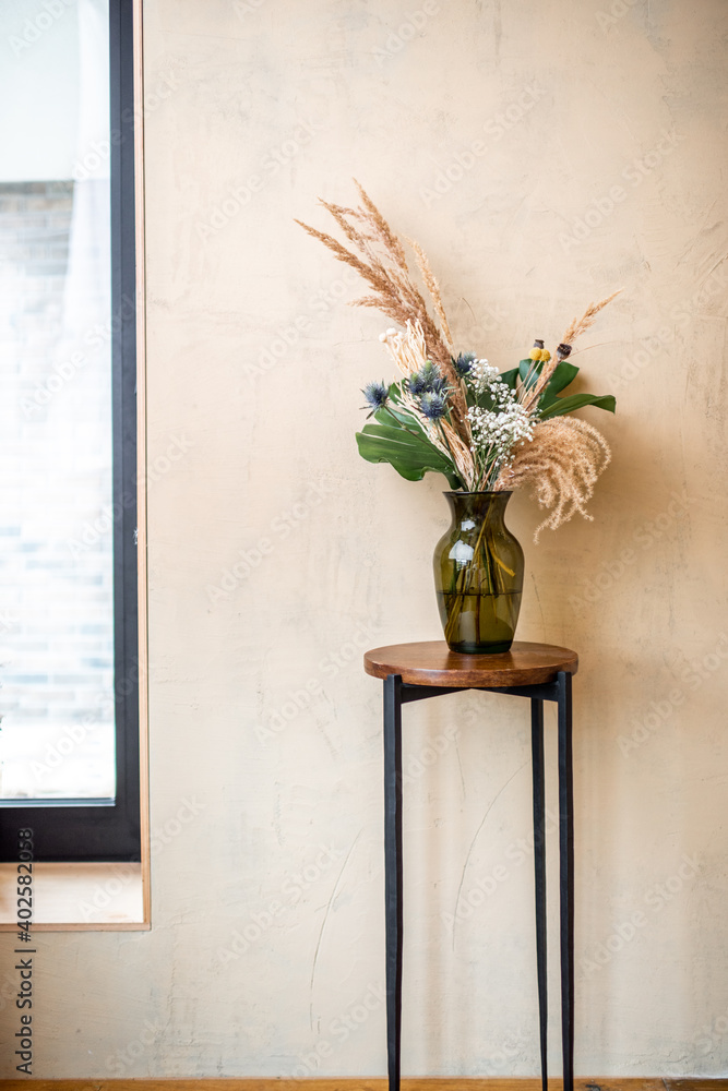 Composition of flowers and herbs in a glass vase on a beige wall background. Bouquet of monstera, Cr