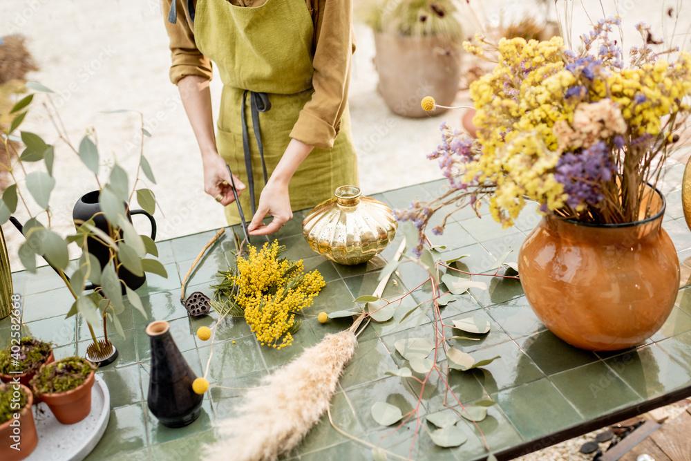 Female making compositions of dried and fresh flowers and herbs on the green table outdoors. Florist