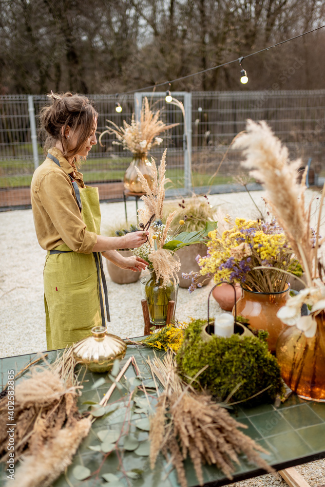 Young woman making compositions of dried and fresh flowers and herbs at the workshop outdoors. Flori