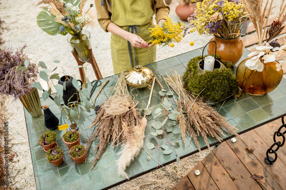 Young woman making compositions of dried and fresh flowers and herbs at the workshop outdoors. Flori