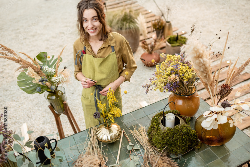 Portrait of a cheerful woman making compositions of dried and fresh flowers and herbs at the worksho