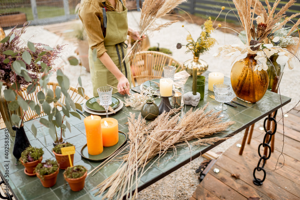 Young female putting herbs on the table, decorating tablescape in natural Boho style in green tones 