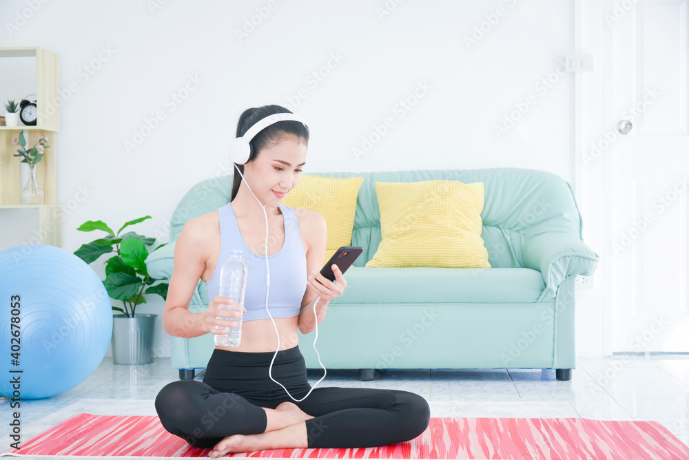 Asian sporty young woman sitting rest and listen music via headphone after doing exercise in living 