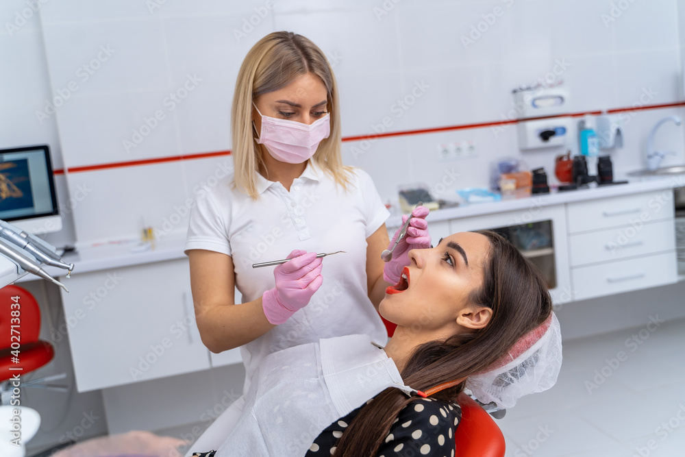 View from side on young female dentist with dentist instruments in hands. Doctor treats patient`s te