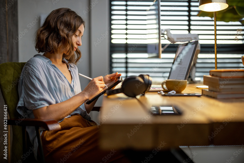 Young woman dressed casually having some creative work, drawing on a digital tablet, sitting at the 