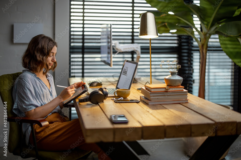 Young woman dressed casually having some creative work, drawing on a digital tablet, sitting at the 