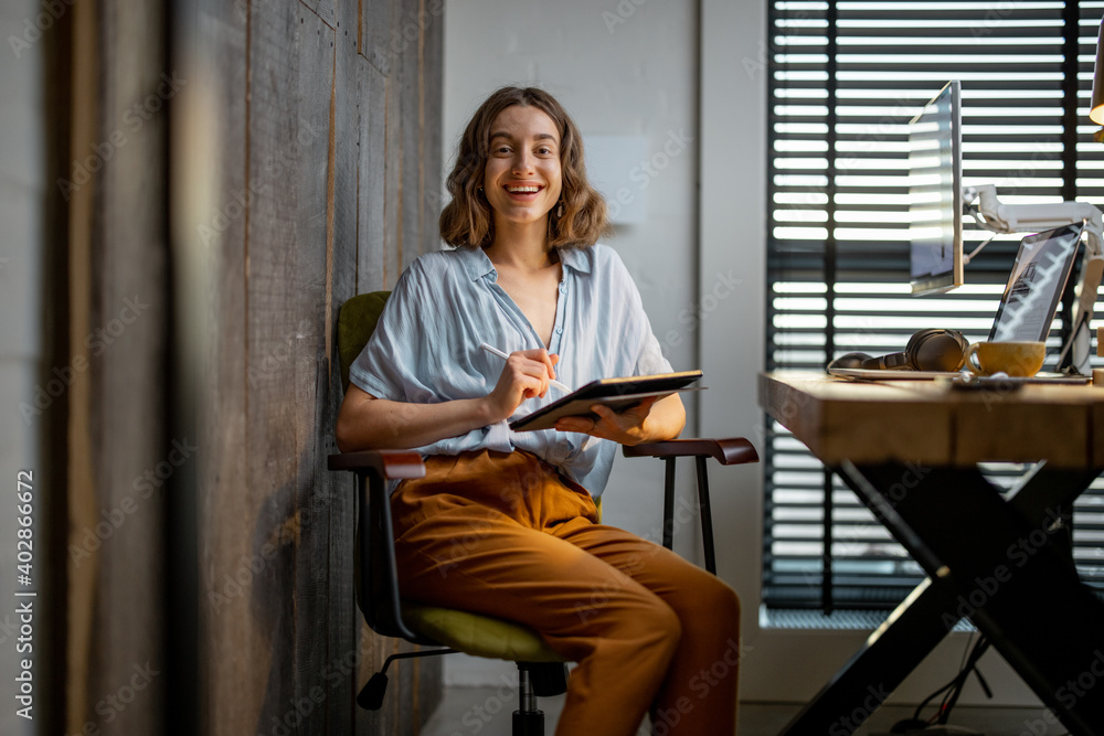 Portrait of a young woman as a digital artist, drawing on a digital tablet at the cozy workplace at 