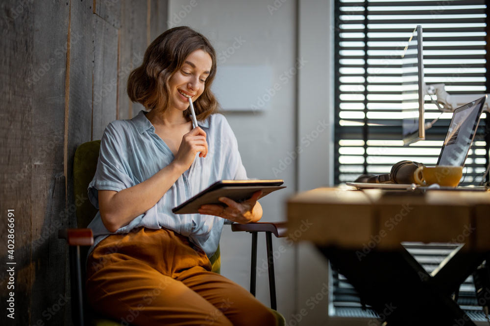 Young woman dressed casually having some creative work, drawing on a digital tablet, sitting at the 