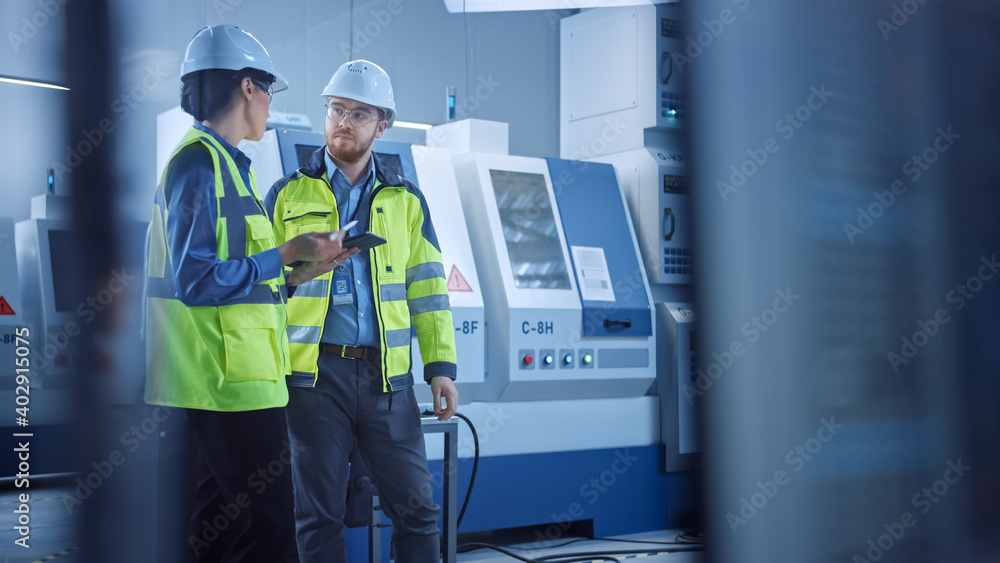 Modern Factory: Female Project Manager and Male Engineer Standing Wearing Safety Jackets and Hard Ha