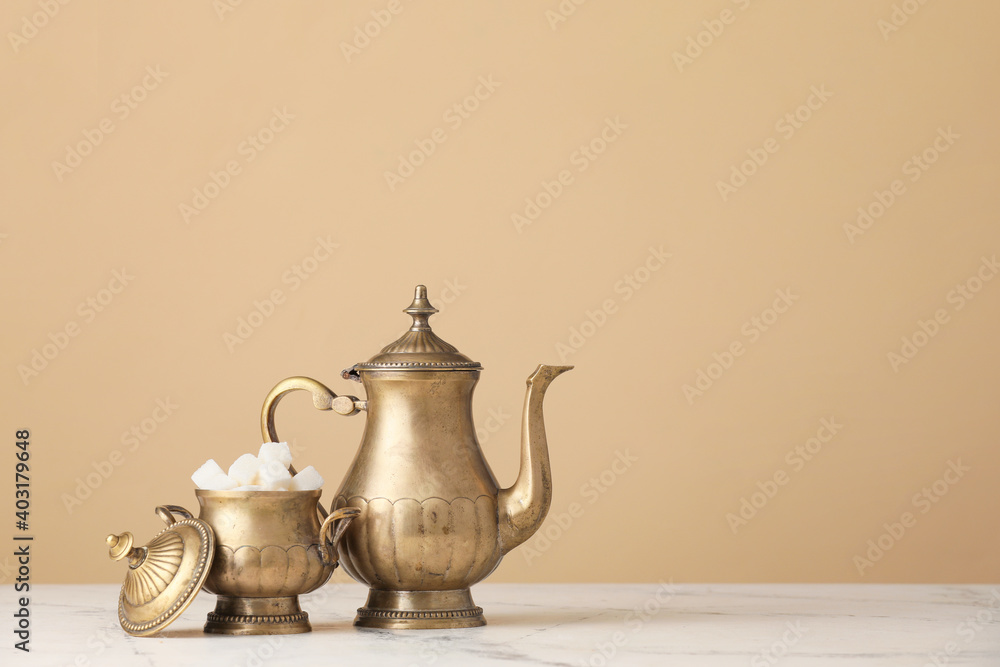 Teapot and sugar bowl on table against color background