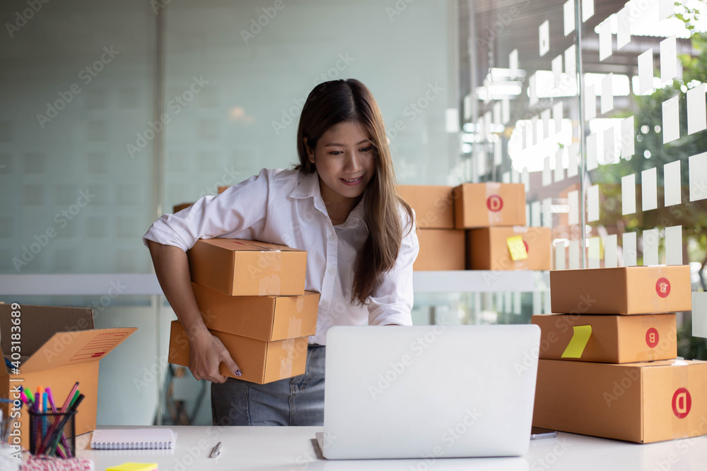 An Asian owner holds a package in a brown box, ready for delivery to a customer who orders online. A