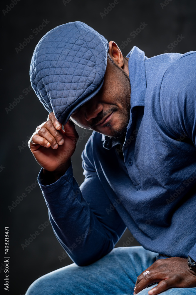 Portrait of a fashionable african american man posing on black background in blue cap and fashion sh