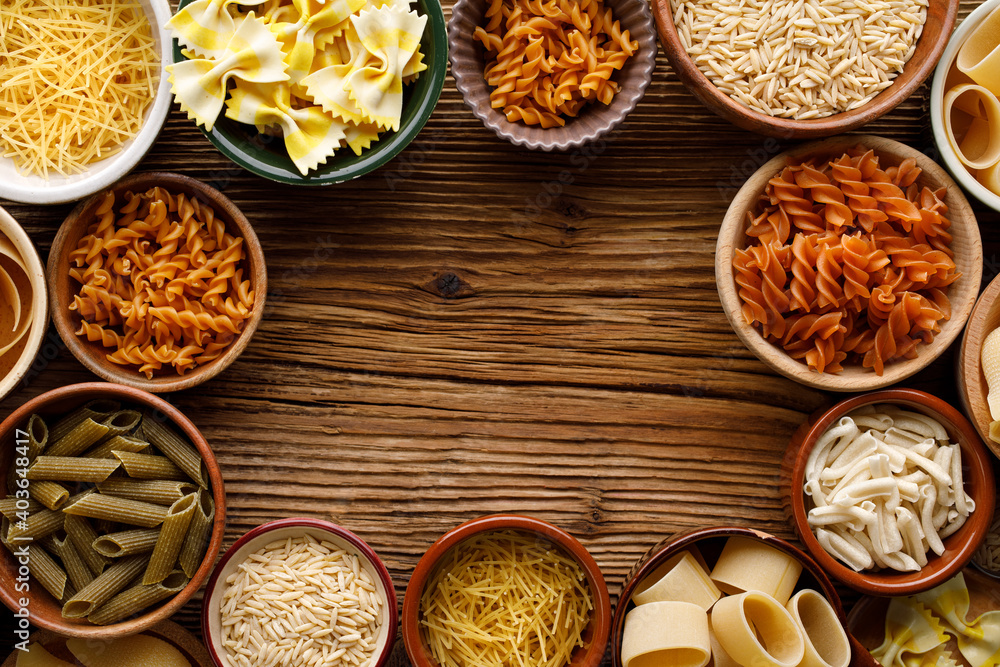 Set of different types of pasta in a bowls on a wooden background with copy space