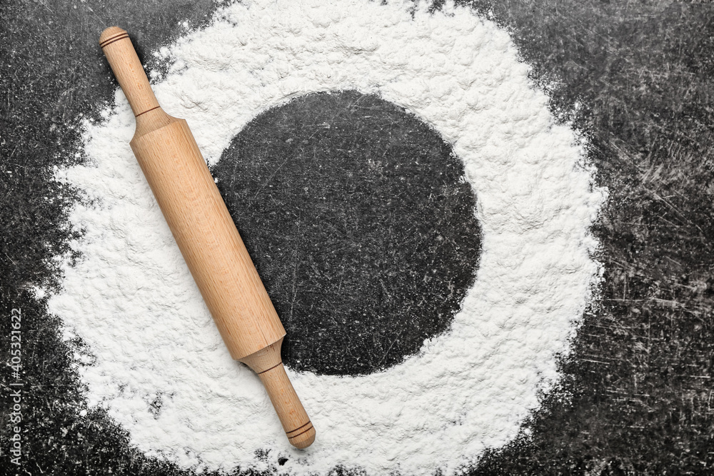 Round frame made of flour and rolling pin on dark background