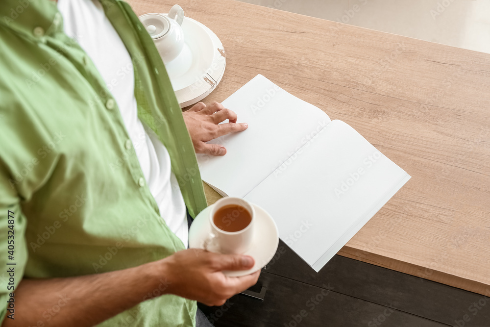 Young man reading magazine and drinking tea at home