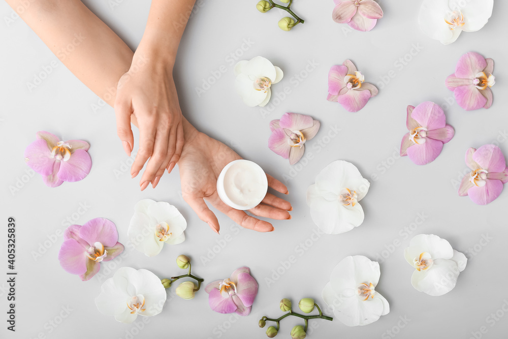 Female hands with cream and beautiful flowers on light background