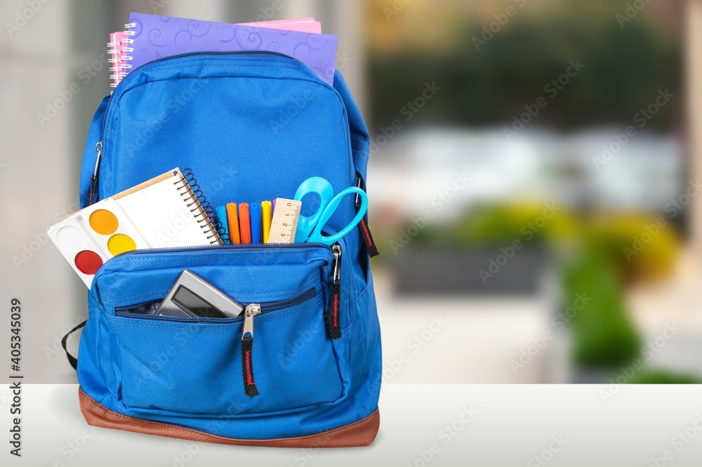 Classic school backpack with colorful school supplies and books on desk.