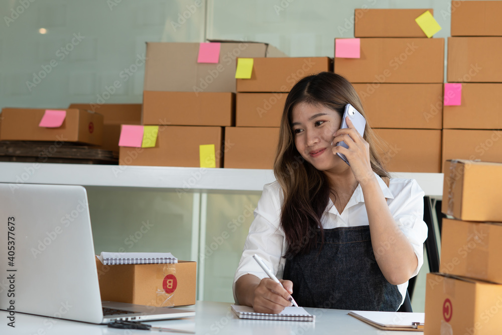 Young Asian entrepreneur owner talking on phone at workplace at home. Start up small business.