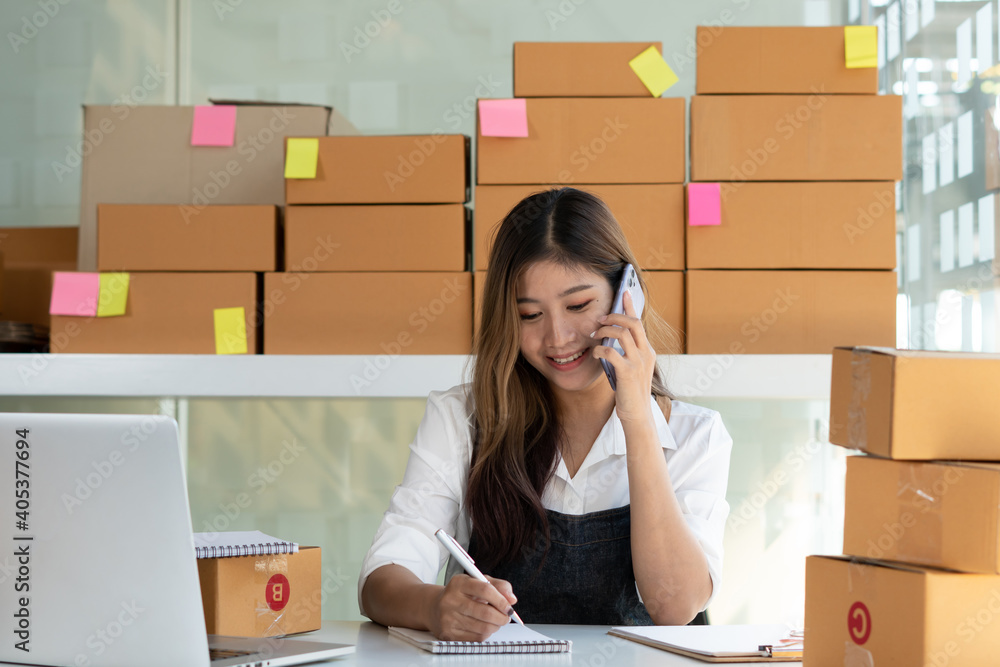 Young Asian entrepreneur owner talking on phone at workplace at home. Start up small business.