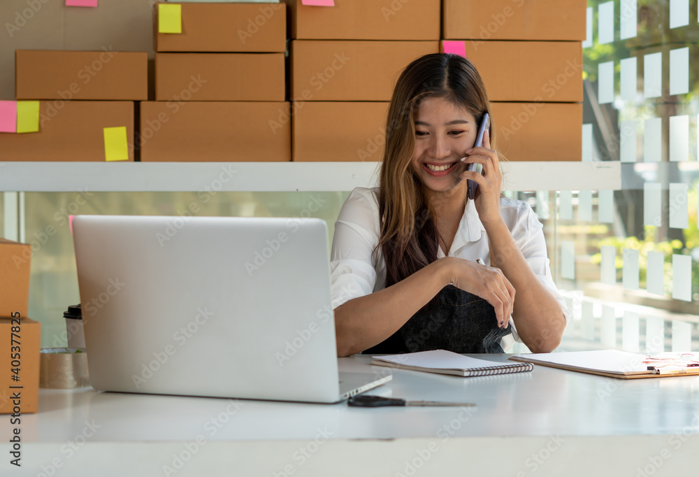 Young Asian entrepreneur owner talking on phone at workplace at home. Start up small business.