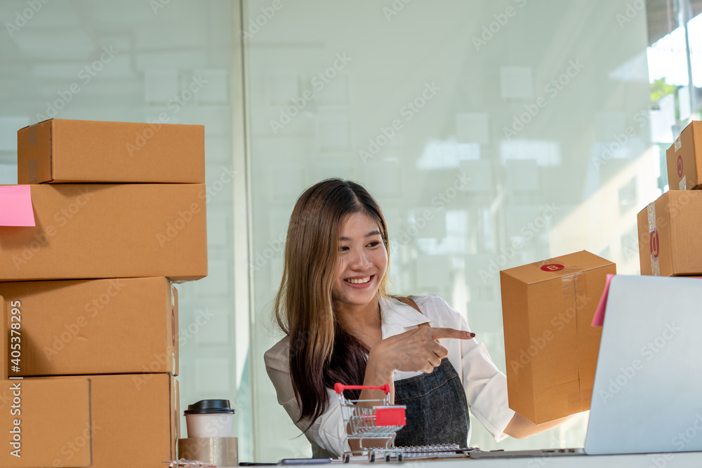 An Asian owner holds a package in a brown box, ready for delivery to a customer who orders online. A