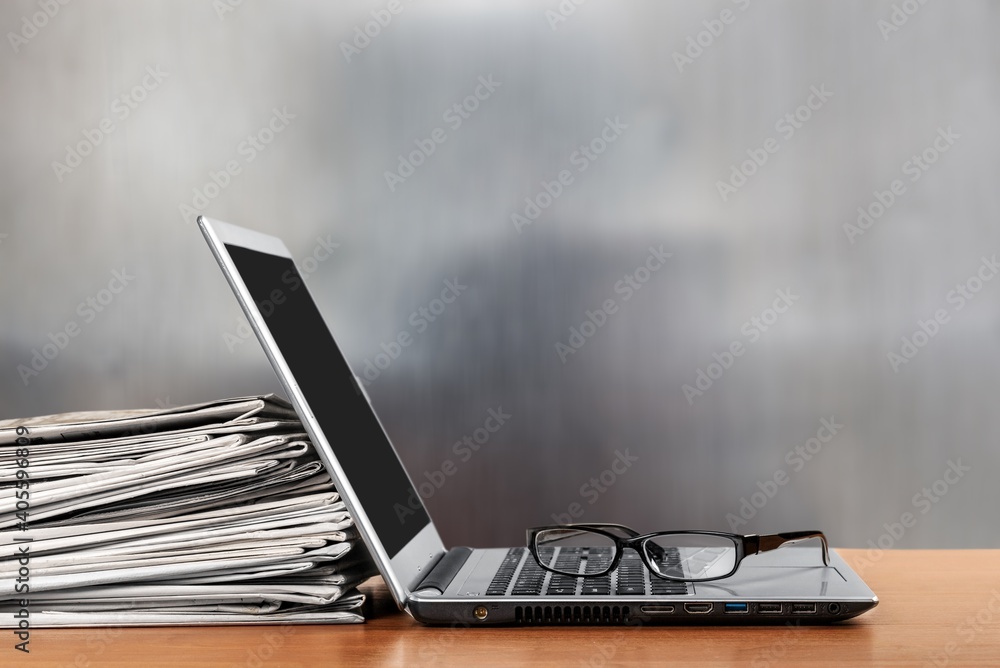 Laptop and newspapers stack on a table with background