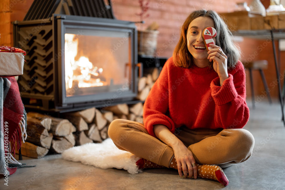 Portrait of a young happy woman with a Christmas candy by the fireplace during winter holidays