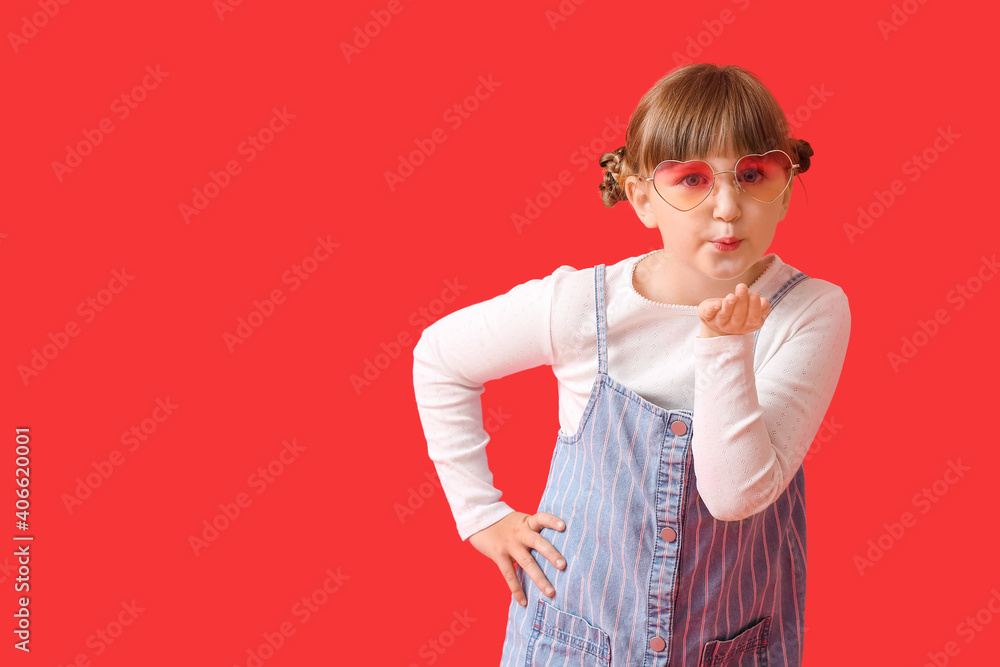 Cute little girl with stylish sunglasses blowing kiss on color background