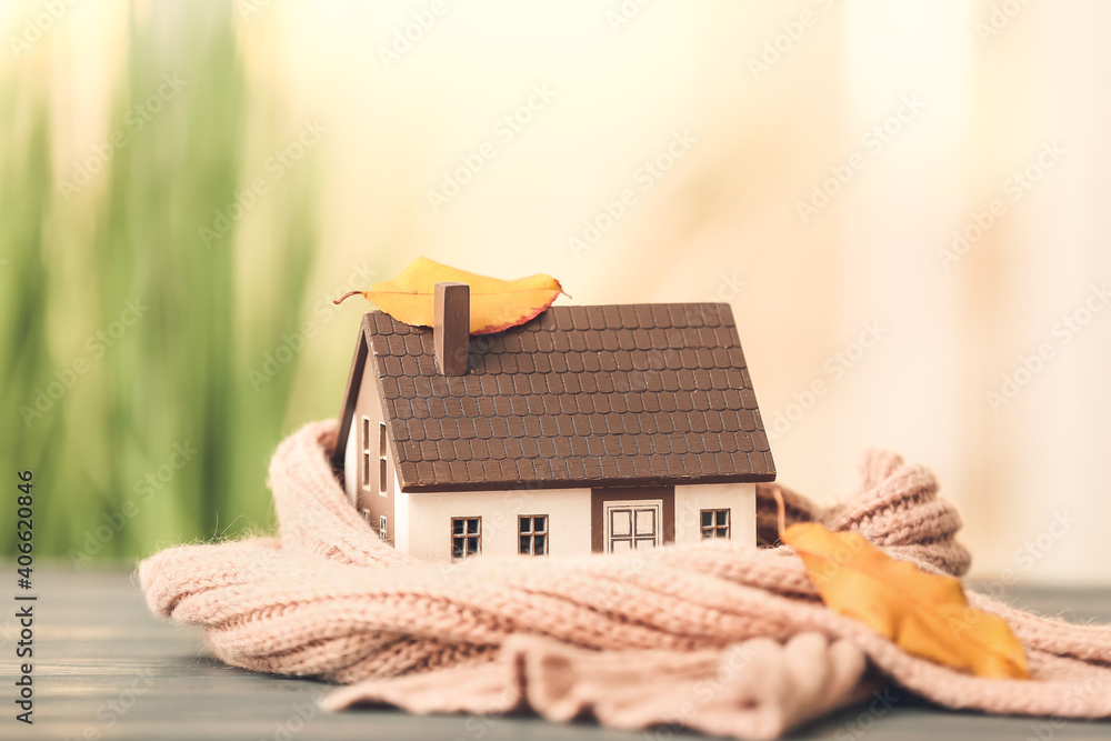 Figure of house, autumn leaves and warm scarf on table. Concept of heating season