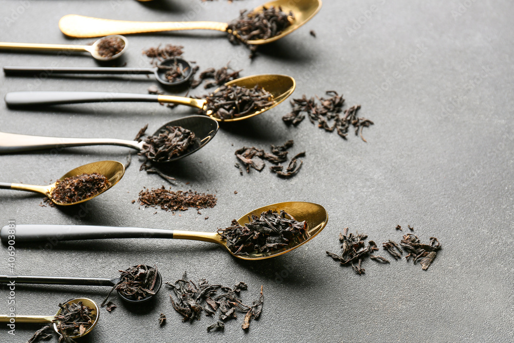 Spoons with dry black tea leaves on dark background