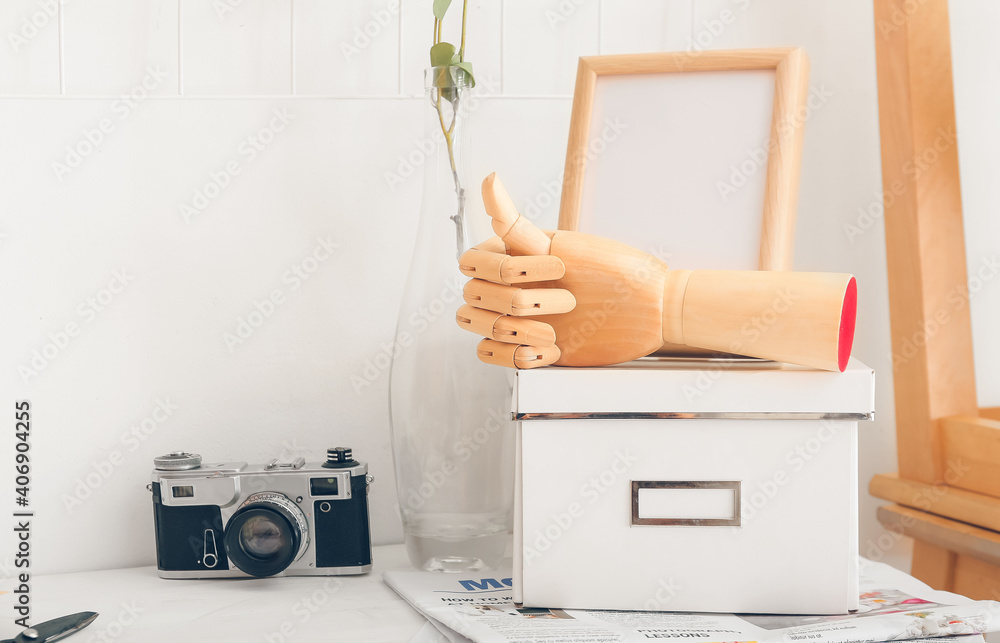 Wooden hand with box and photo camera on table in room