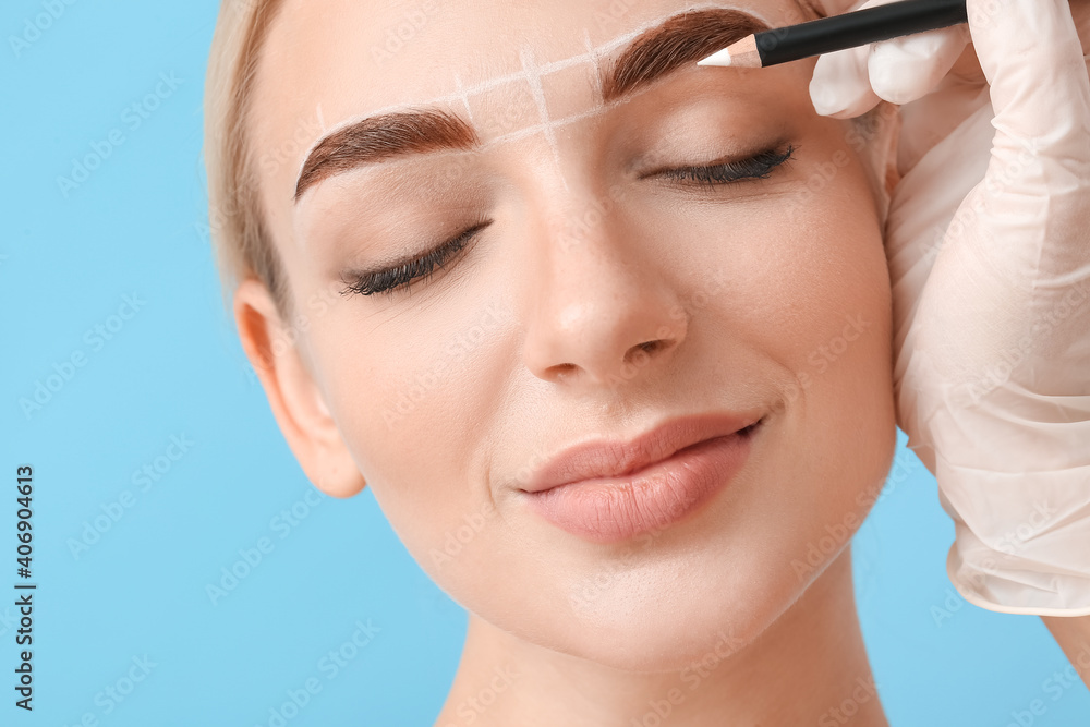 Young woman undergoing eyebrow correction procedure on color background