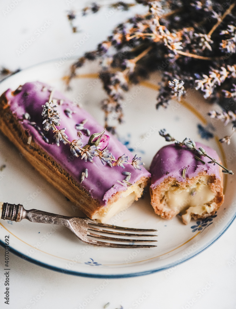 淡紫色eclair，奶油色，紫色花朵装饰，白色m上方椭圆形盘子上有复古叉子