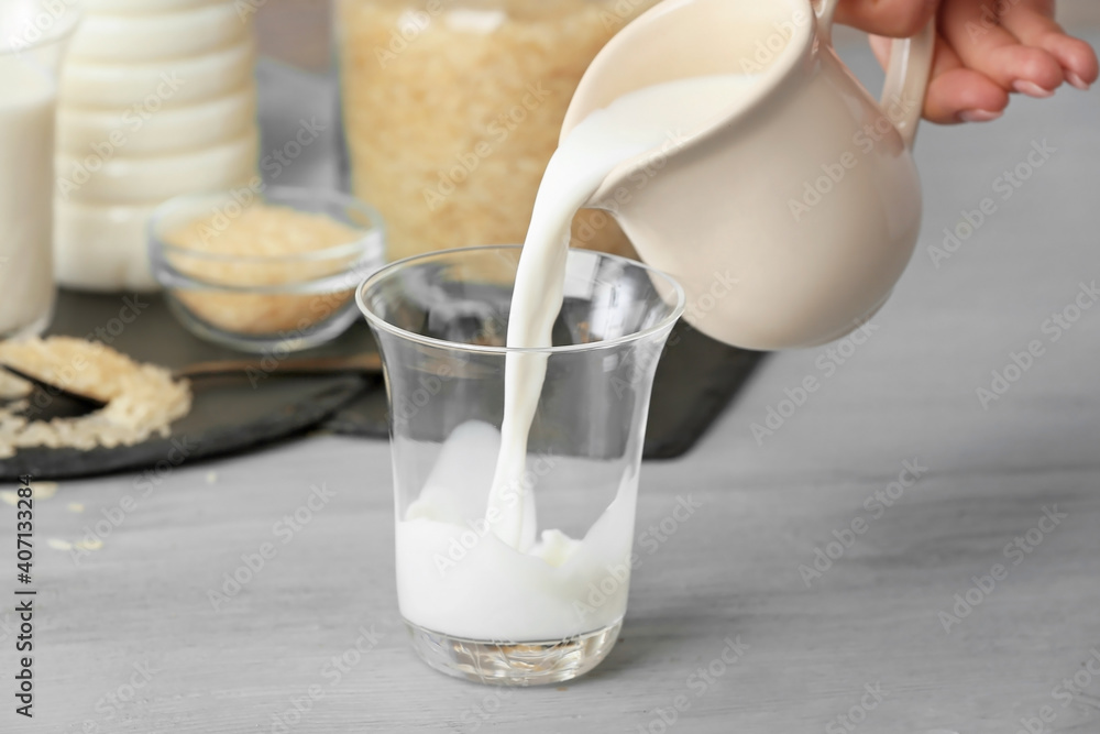 Pouring of rice milk from jug into glass on table