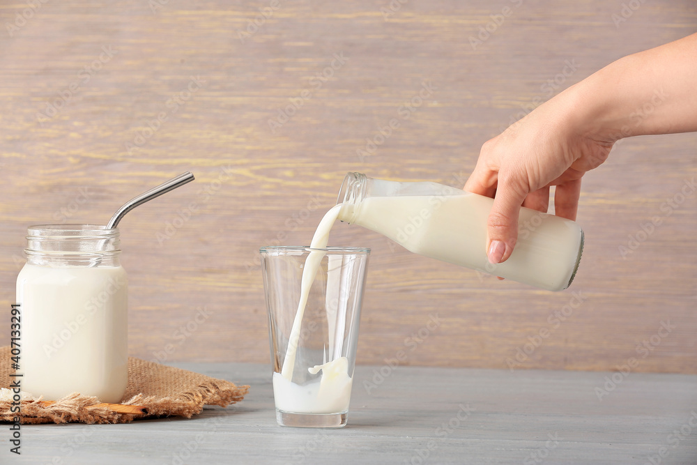 Woman pouring rice milk from bottle into glass on table