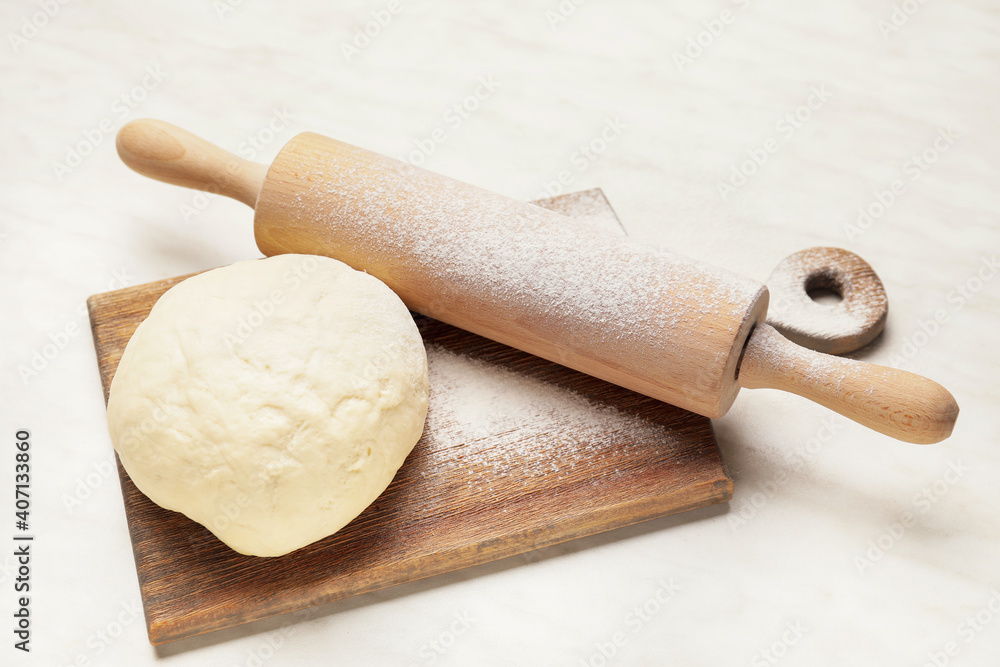 Fresh dough and rolling pin on light background